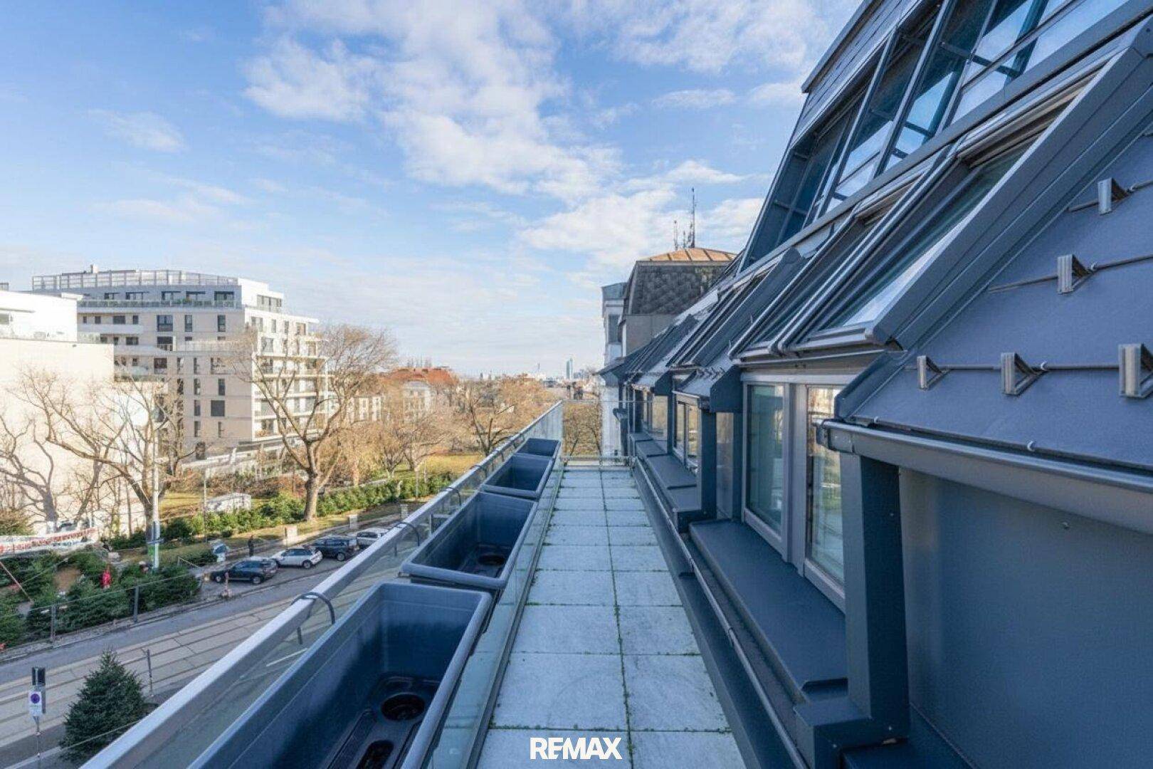 Langer, schmaler Balkon mit Fliesenboden und Blick auf die umliegenden Gebäude und Straßen.