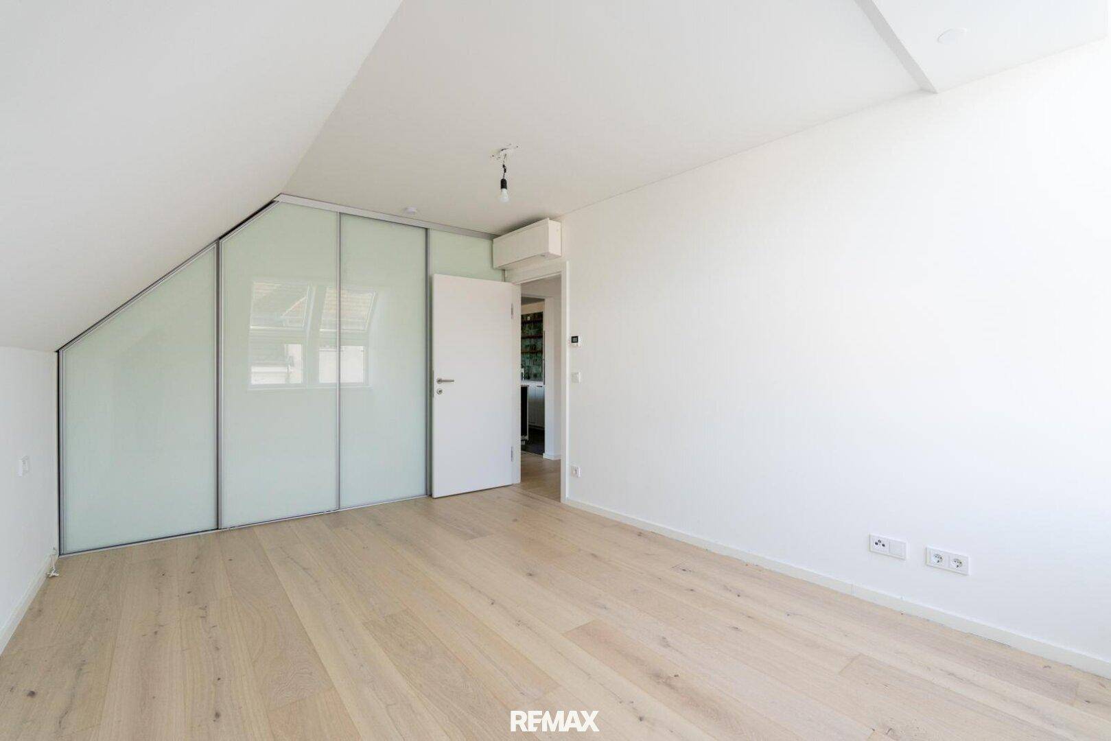 Schlafzimmer mit Dachschrägen, hellem Parkettboden und integrierten Schiebetürenschränken.