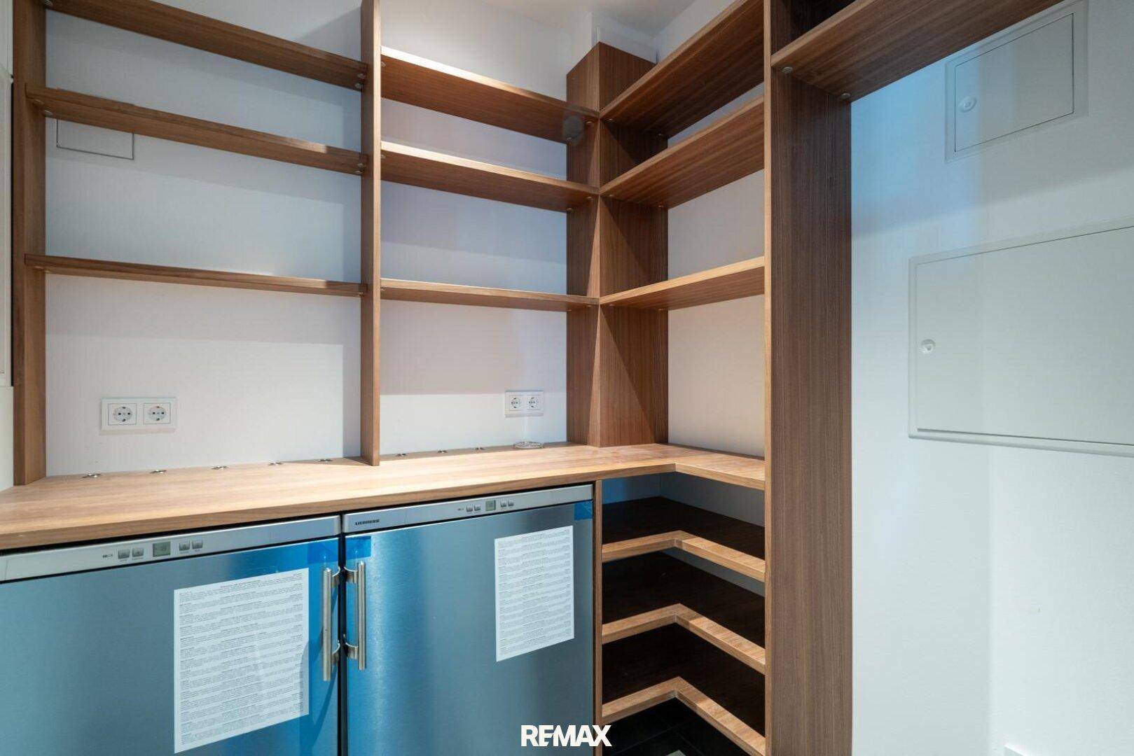 Praktischer Abstellraum mit Holzregalen und integrierten Kühl- oder Gefrierschränken.