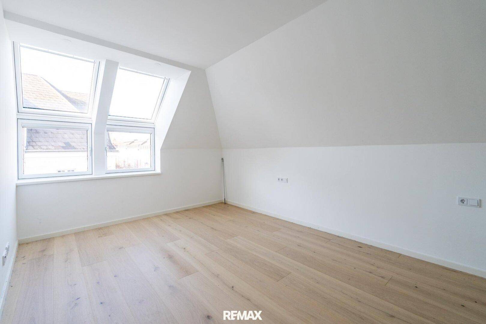 Helles Schlafzimmer mit Dachschrägen, großen Dachfenstern und hellem Holzfußboden.