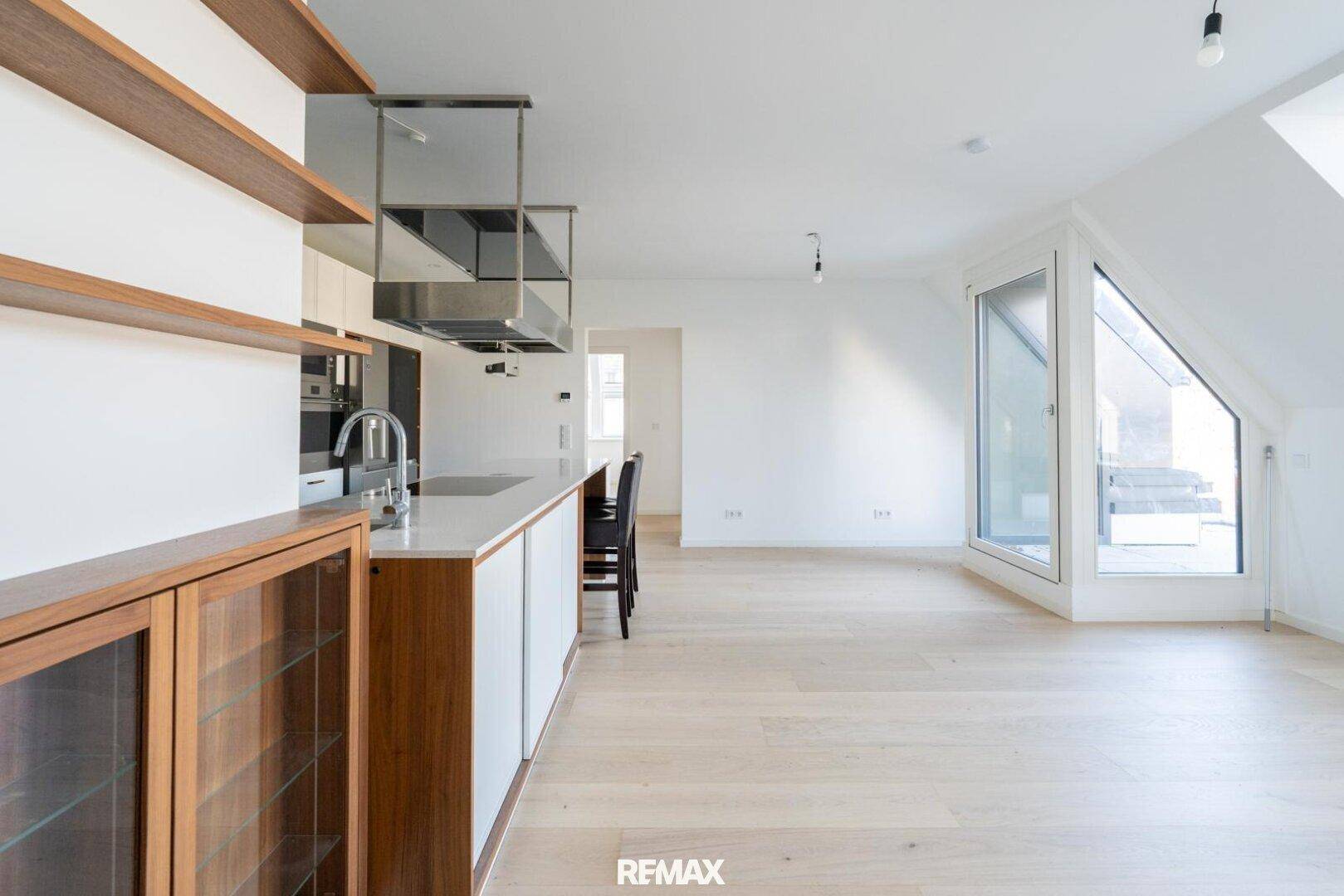 Offener Wohnbereich mit hellem Parkettboden, Dachschrägen und Zugang zu einem Balkon.