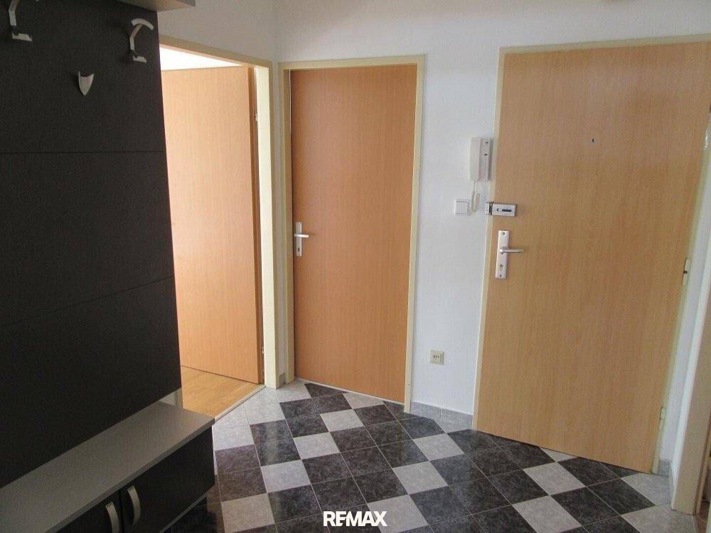 Eingangsbereich mit kariertem Fliesenboden, Garderobe und mehreren Holztüren.