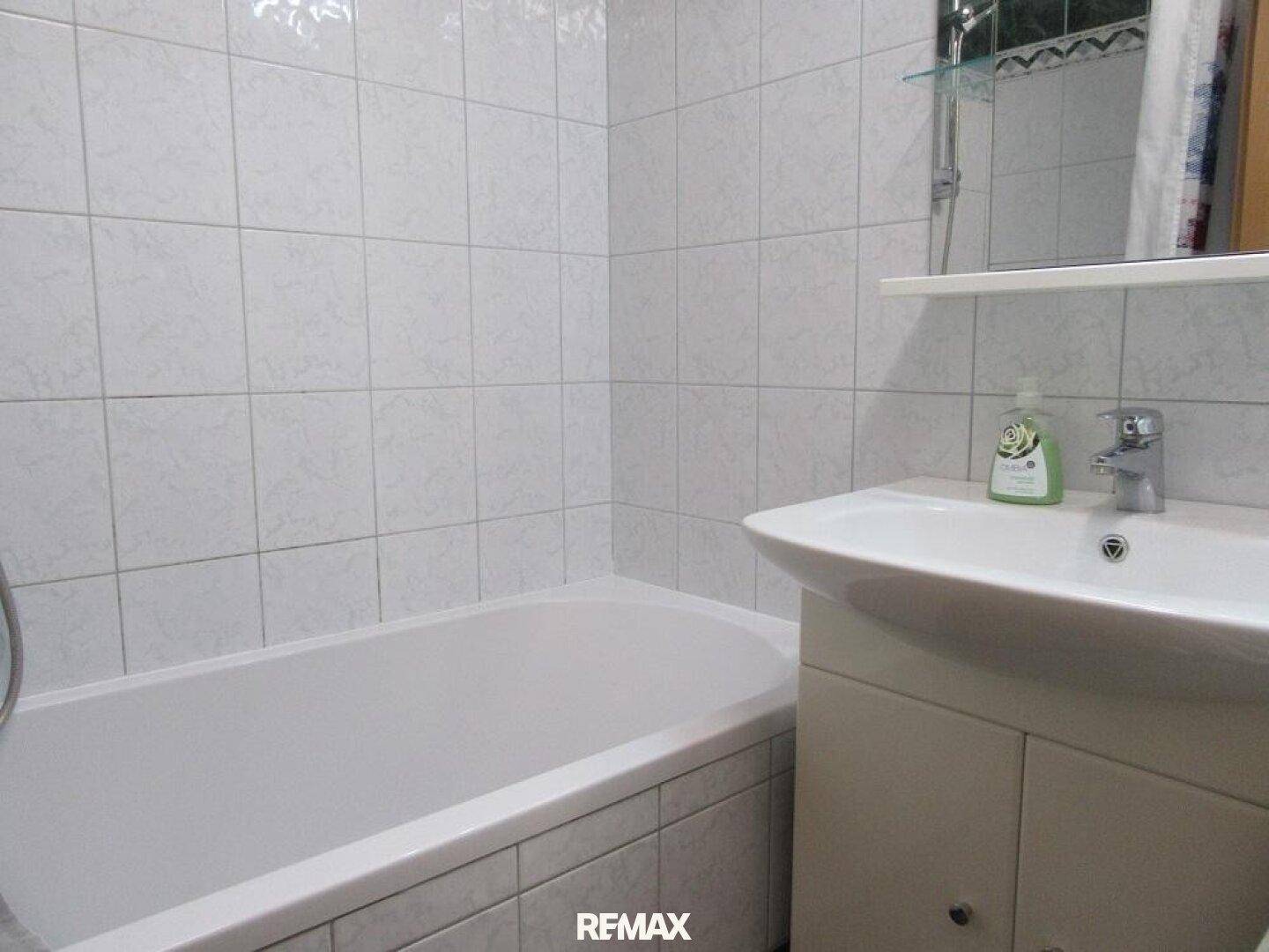 Badezimmer mit weißen Fliesen, Badewanne und Waschbecken mit Unterschrank.