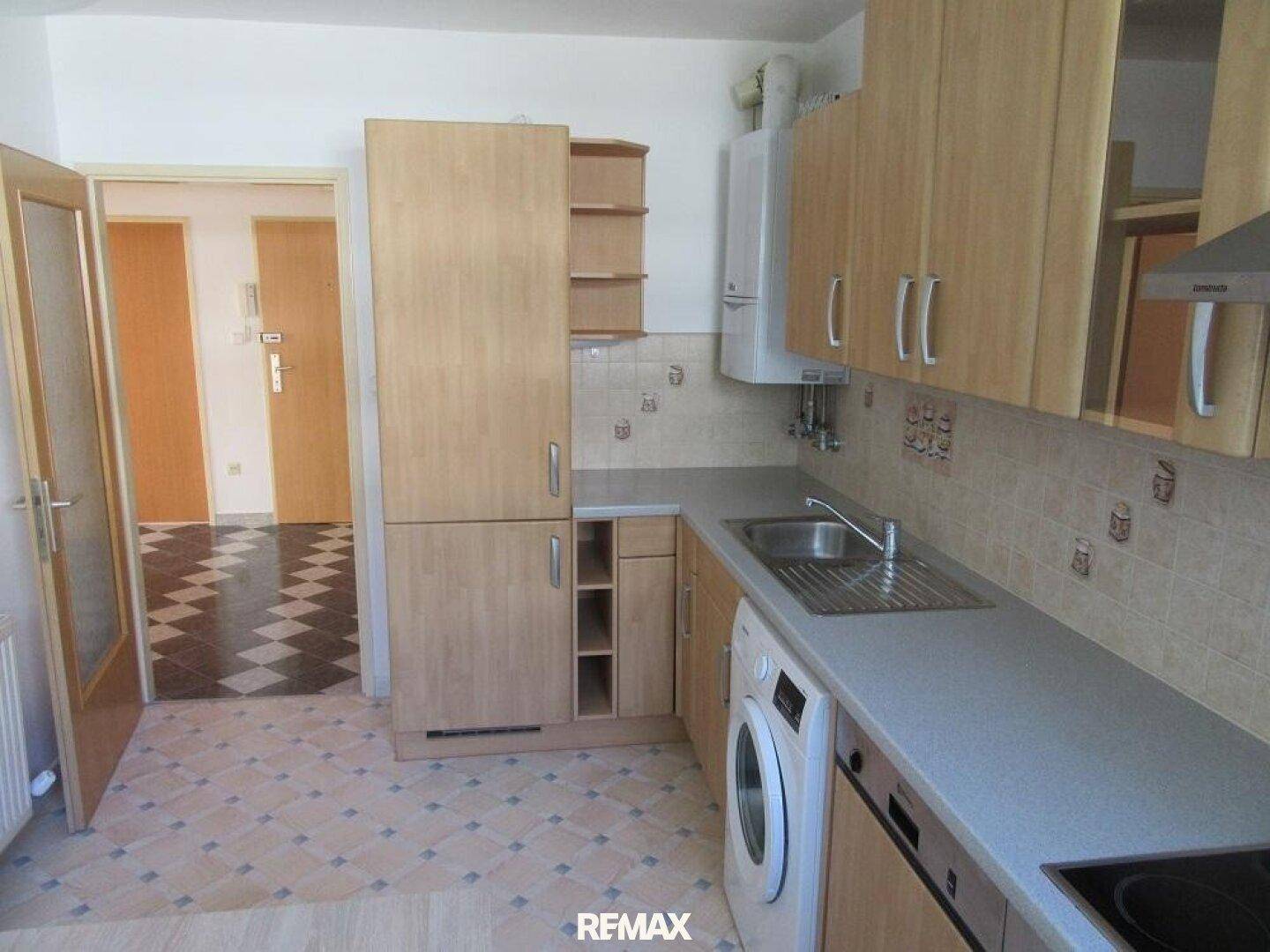 Funktionale Küche mit Holzschränken, Spüle, Waschmaschine und gefliestem Boden.