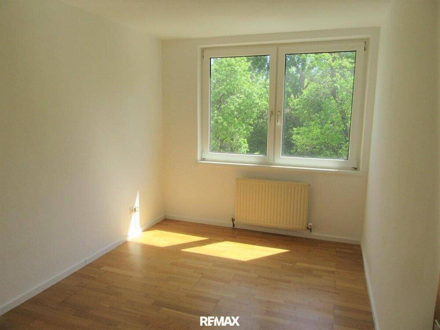 Helles Schlafzimmer mit Parkettboden und Ausblick ins Grüne durch das Fenster.