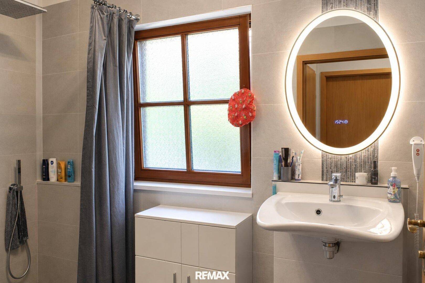 Modernes Badezimmer mit Waschtisch, beleuchtetem Spiegel und Fenster für Tageslicht.