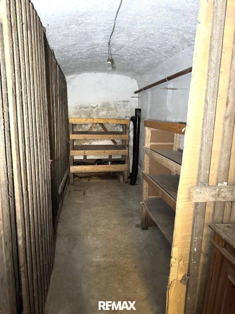 Unausgebauter Kellerraum mit einfachen Holzregalen und Betonboden, ideal als Lagerfläche.