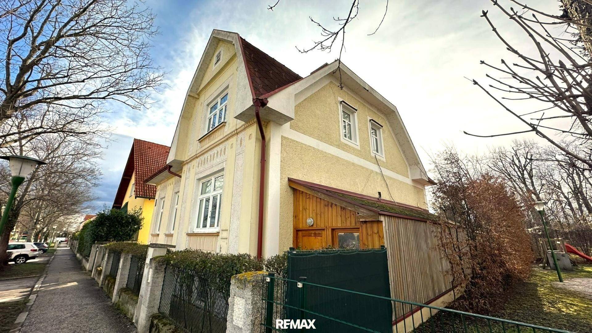 Seitenansicht des Hauses von der Straße, mit gelber Fassade, rotem Dach und einem Holzanbau im Winter.