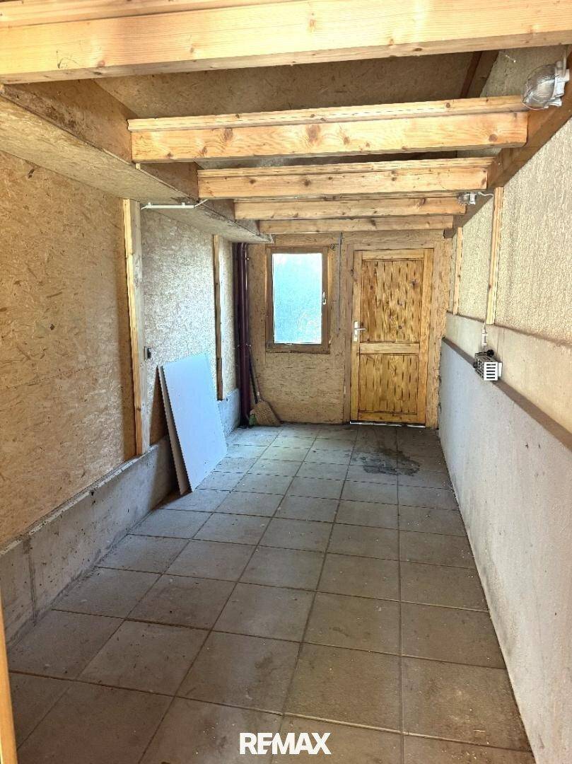 Unfertiger Raum mit Fliesenboden, sichtbaren Holzdeckenbalken und einem Fenster, nutzbar als Werkstatt.
