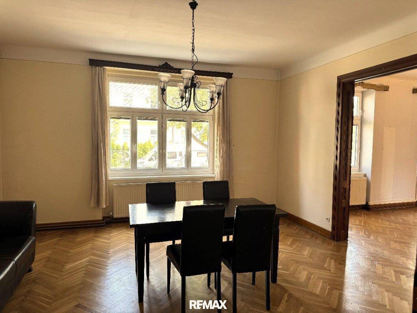 Helles Esszimmer mit Fischgrätparkett, einem dunklen Esstisch und Blick ins Grüne durch das große Fenster.