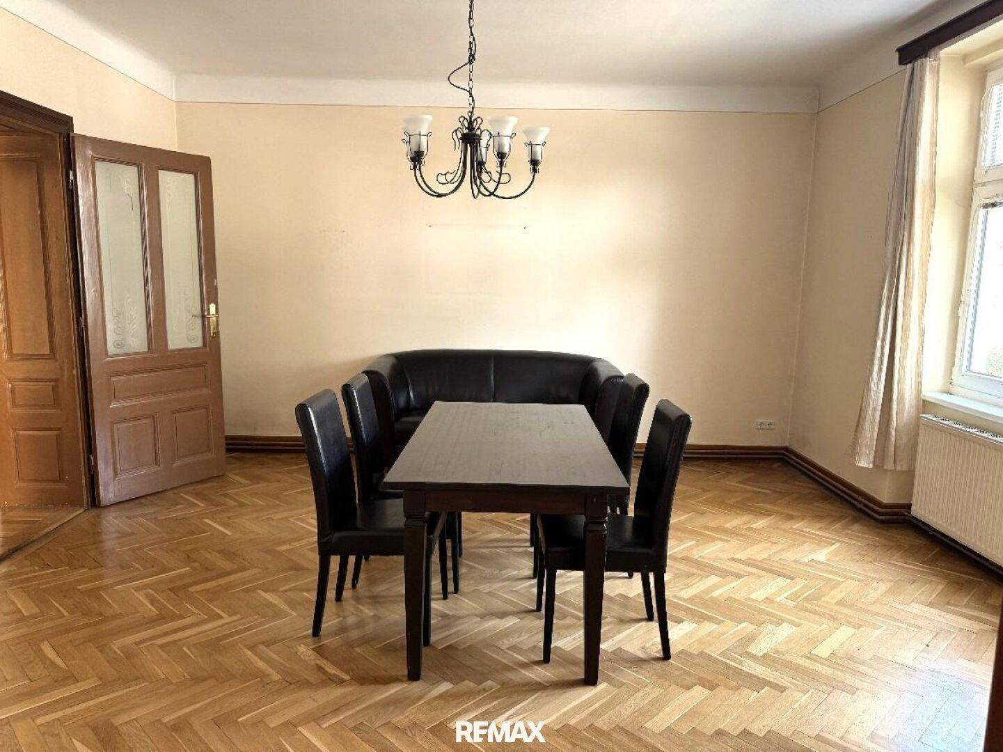 Esszimmer mit Fischgrätparkett, einem dunklen Esstisch und passenden Stühlen sowie einer geschwungenen Sitzbank.