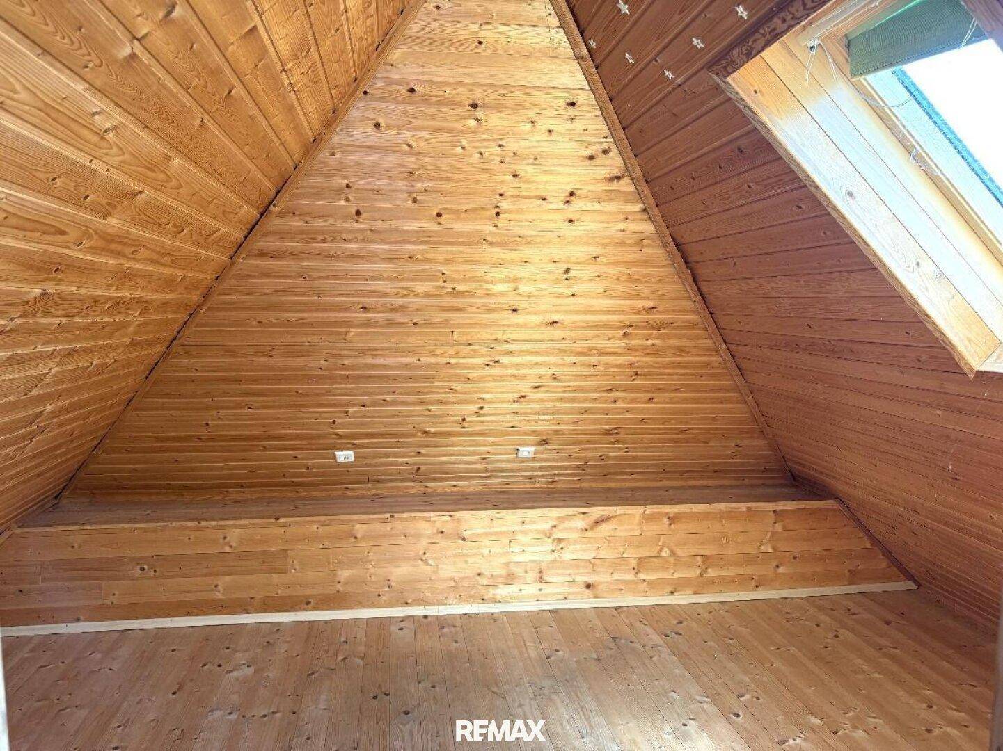 Dachzimmer mit vollständig holzvertäfelten Wänden und Decke, einem hohen Gewölbe und Dachfenster.