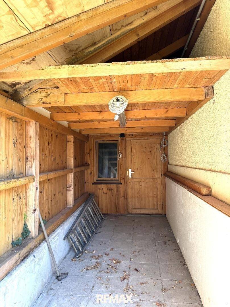 Überdachter Außenbereich mit Fliesenboden, Holzwänden und sichtbaren Deckenbalken, ideal zum Entspannen.