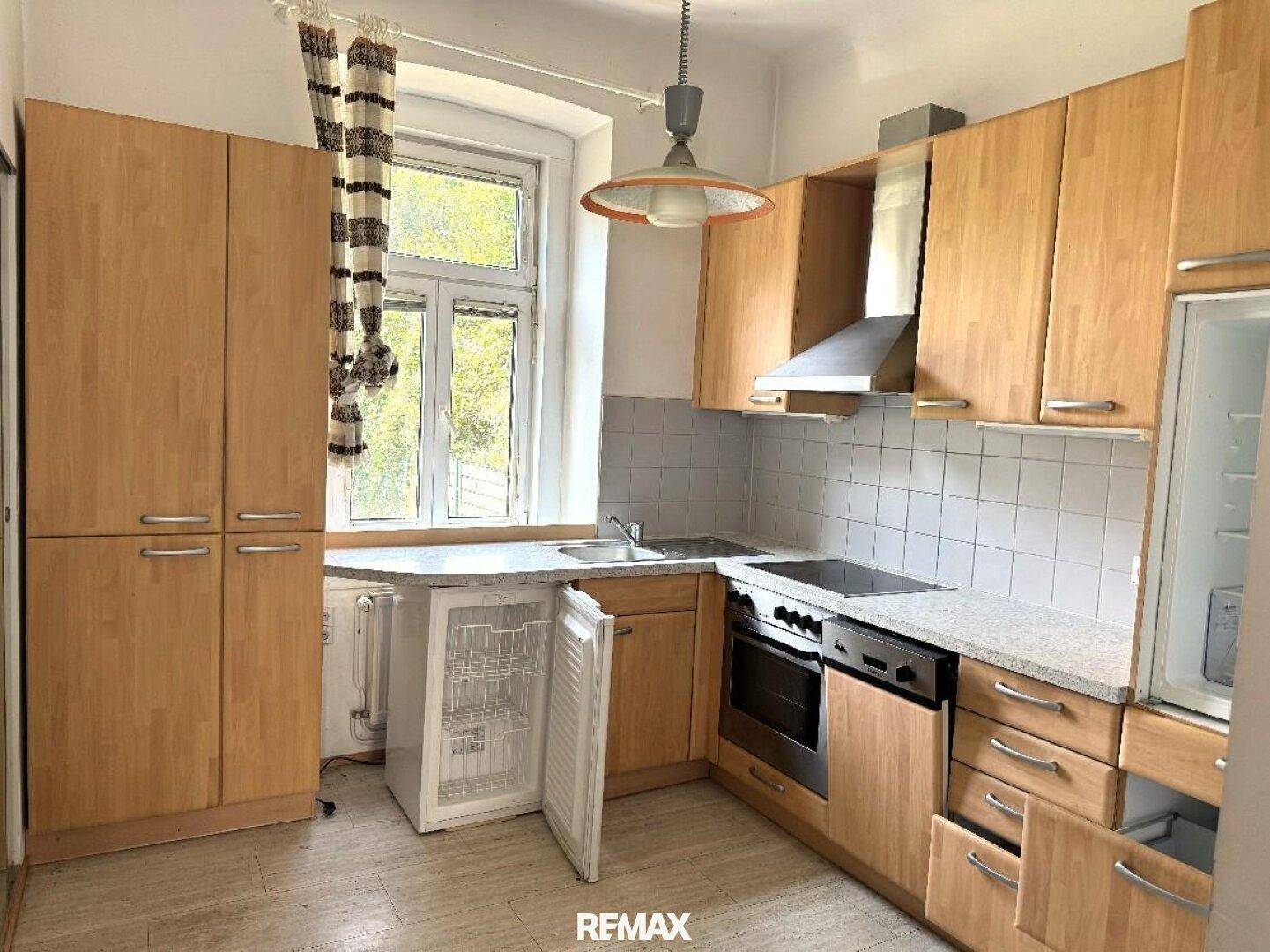 Funktionale Küche mit hellen Holzschränken, weiß gefliestem Spritzschutz und einem Fenster über der Spüle.