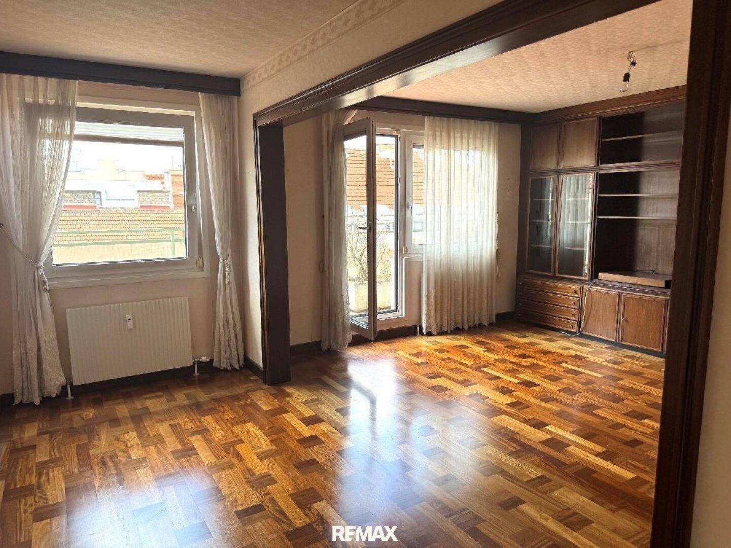 Geräumiges Wohnzimmer mit Fischgrätparkett, Holzvertäfelung und Zugang zu einem Balkon.