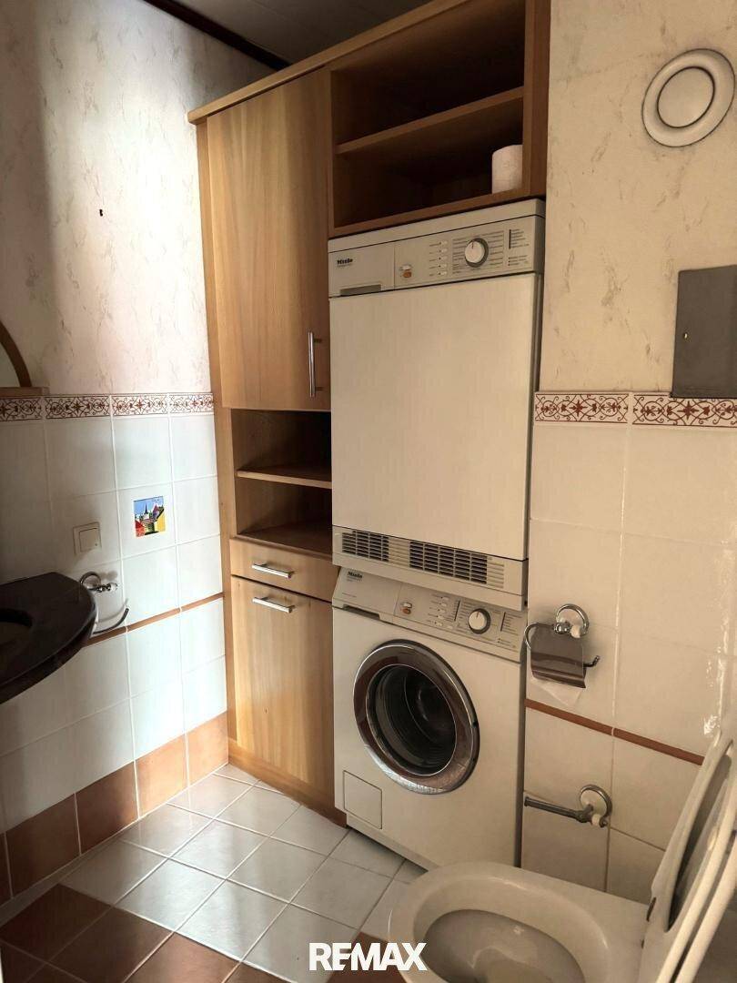 Separates WC mit Waschmaschine, Trockner und praktischen Holzschränken für zusätzlichen Stauraum.