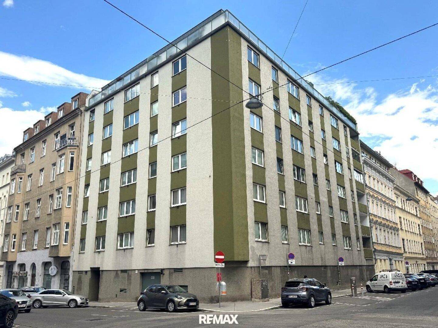 Mehrstöckiges Wohngebäude an einer Straßenecke mit grüner und beiger Fassade in der Stadt.