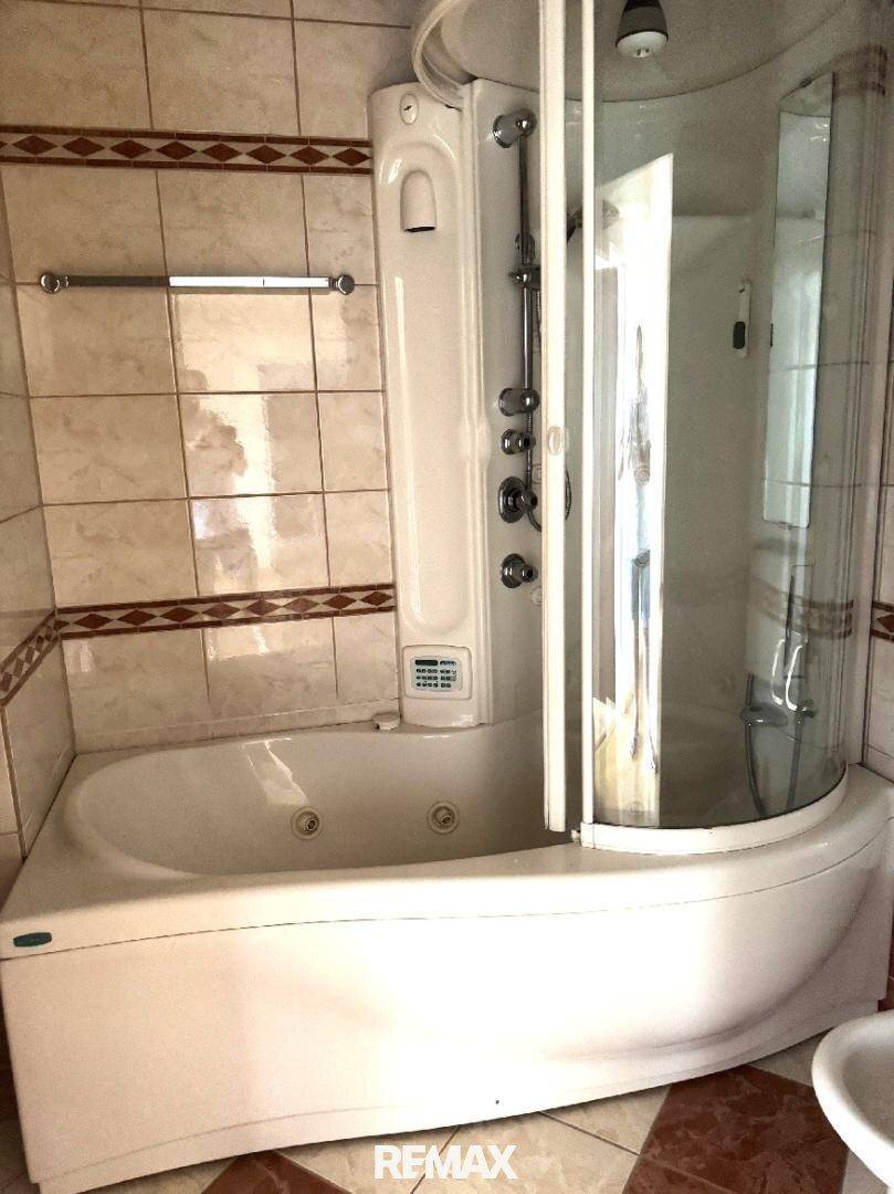 Badezimmer mit Eckbadewanne und integrierter Duschkabine, gefliesten Wänden und Boden.