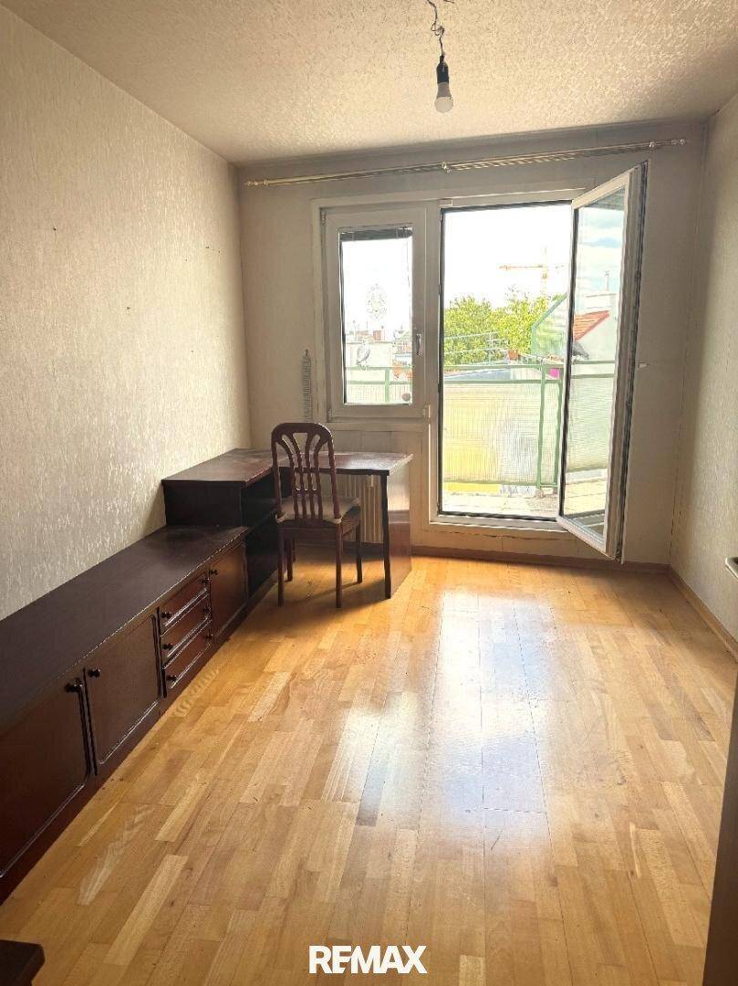 Helles Zimmer mit Holzfußboden, einem Schreibtisch und Zugang zu einem sonnigen Außenbereich.
