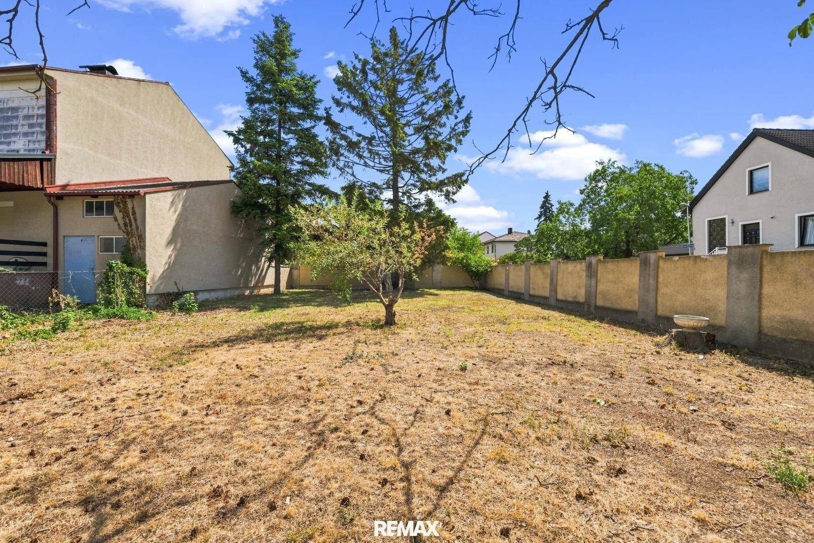 Weitläufiger Garten mit Rasenfläche, Bäumen und umzäuntem Grundstück.