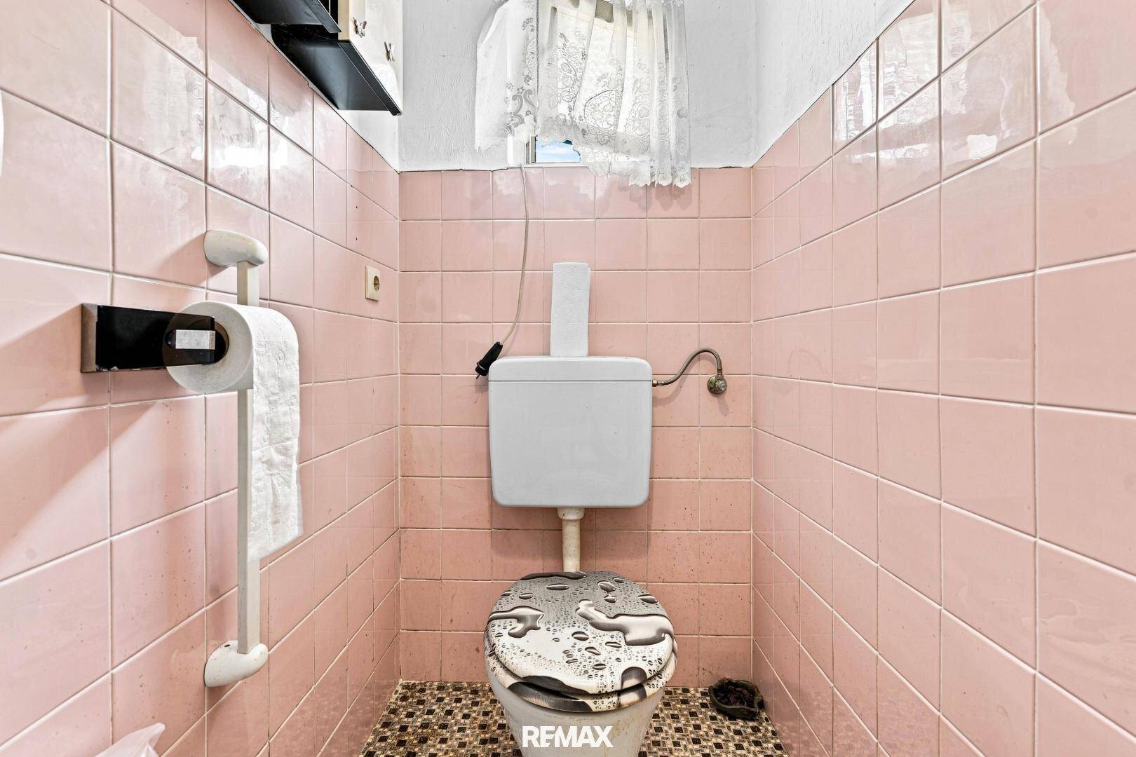 Separate Toilette mit rosa Fliesen und einem Fenster.