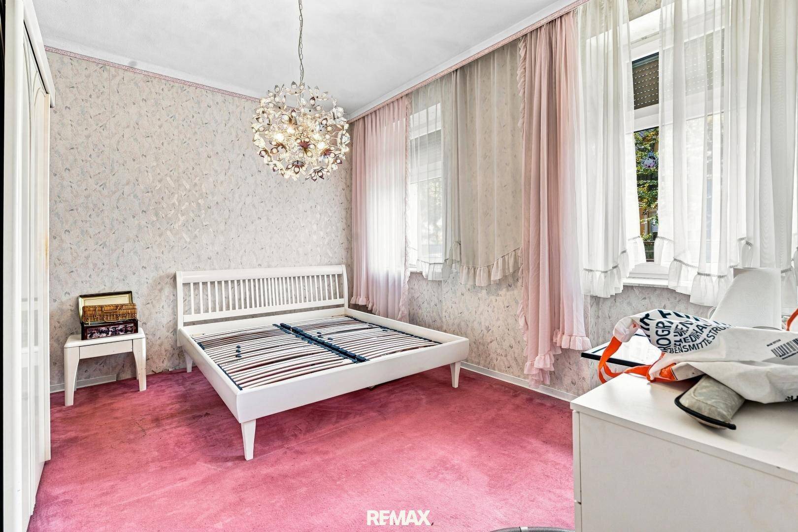 Schlafzimmer mit rosa Teppichboden, weißem Bettrahmen und einem Kronleuchter.