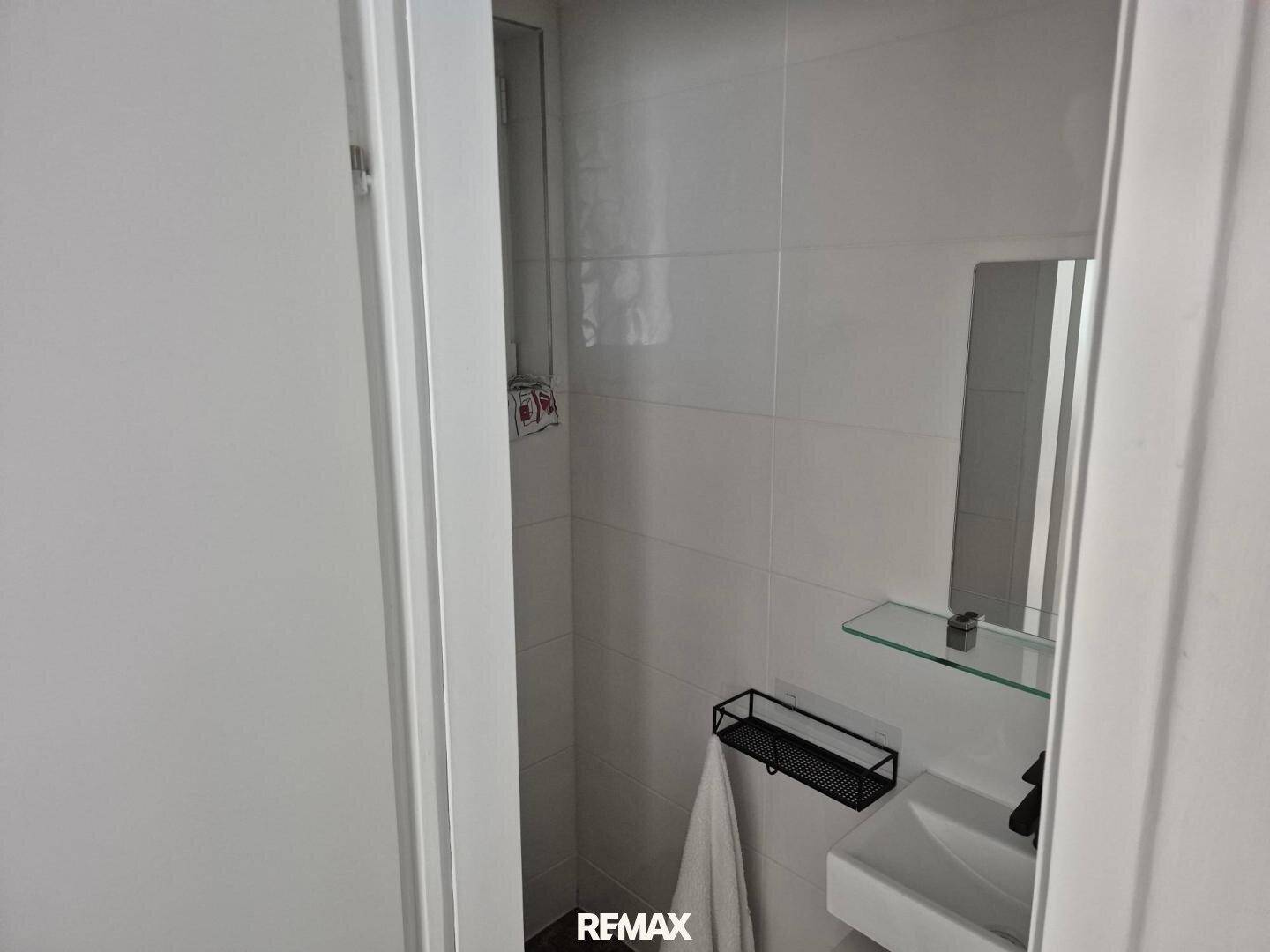 Kleines, hell gefliestes WC mit Waschbecken und Spiegel, funktional und sauber.