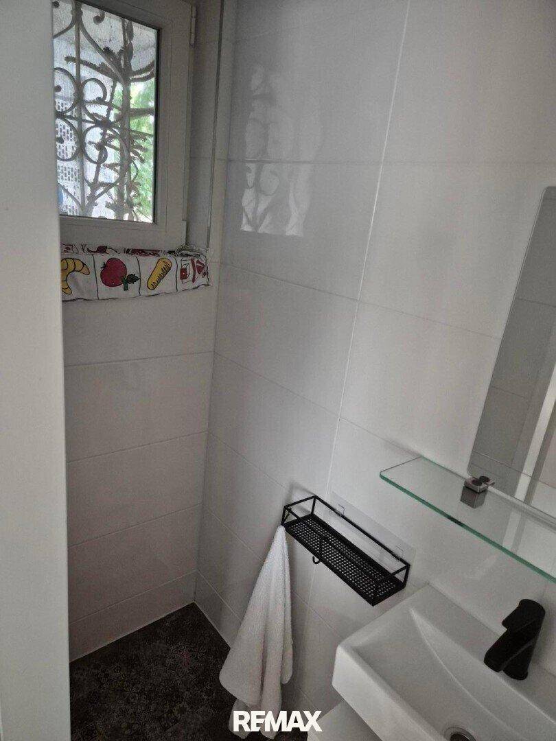 Kleines WC mit Waschbecken, Spiegel und Fenster, das für natürliche Belüftung sorgt.