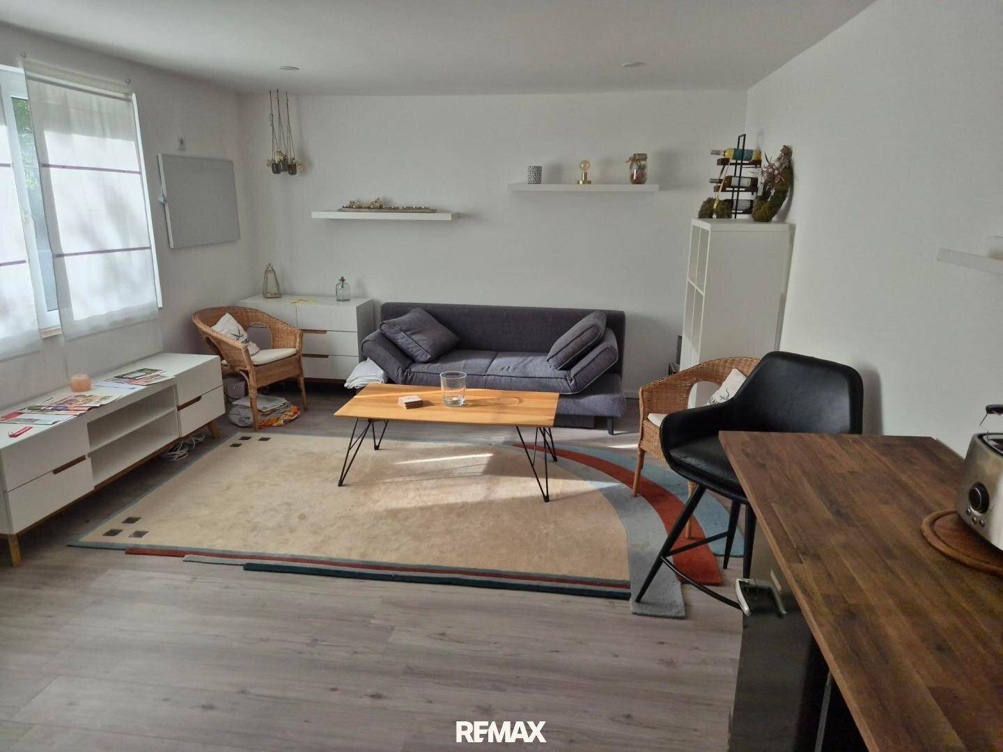 Gemütliches Wohnzimmer mit Sofa, Couchtisch und großem Fenster, das viel Tageslicht hereinlässt.