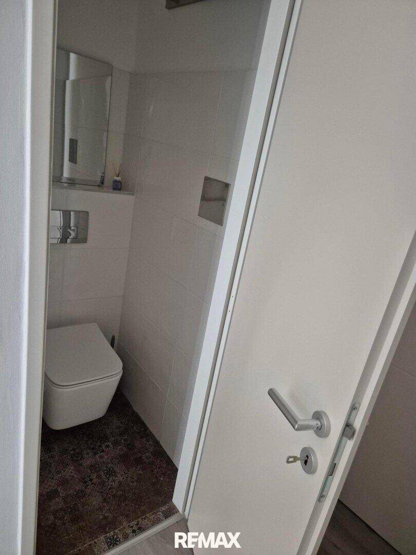 Modernes WC mit wandhängender Toilette und kleinem Teppich, sauber und funktional gestaltet.