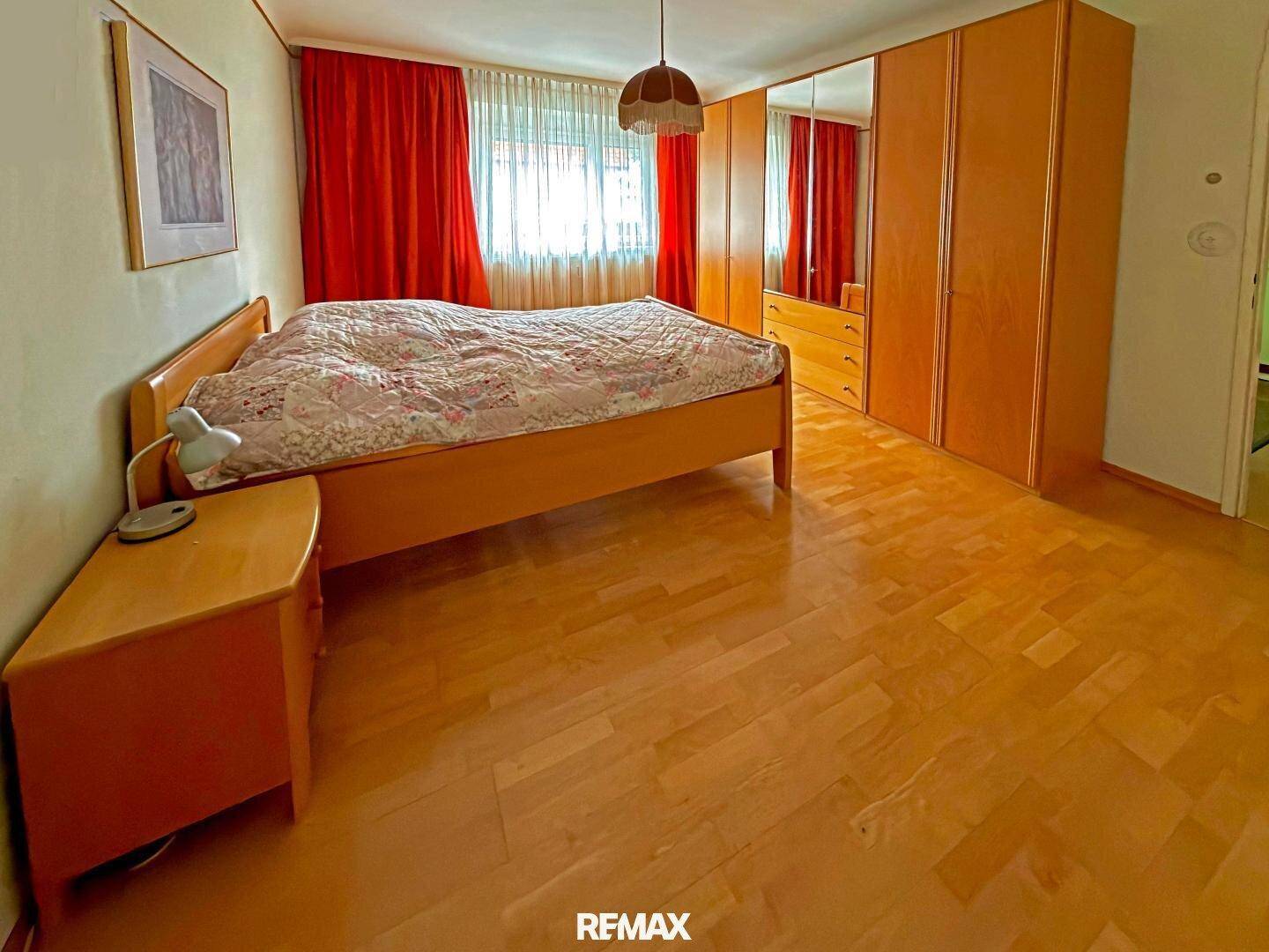 Schlafzimmer mit Holzbett, Nachttisch und großem Kleiderschrank mit Spiegeltüren.