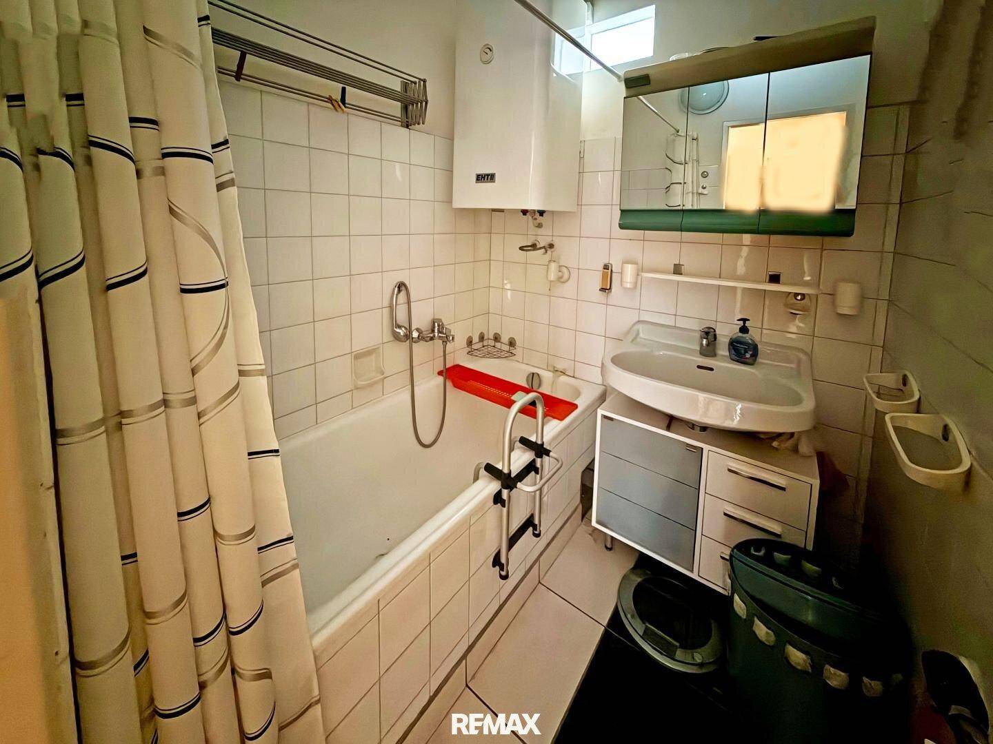 Badezimmer mit Badewanne, Waschbecken, Spiegelschrank und gefliesten Wänden.
