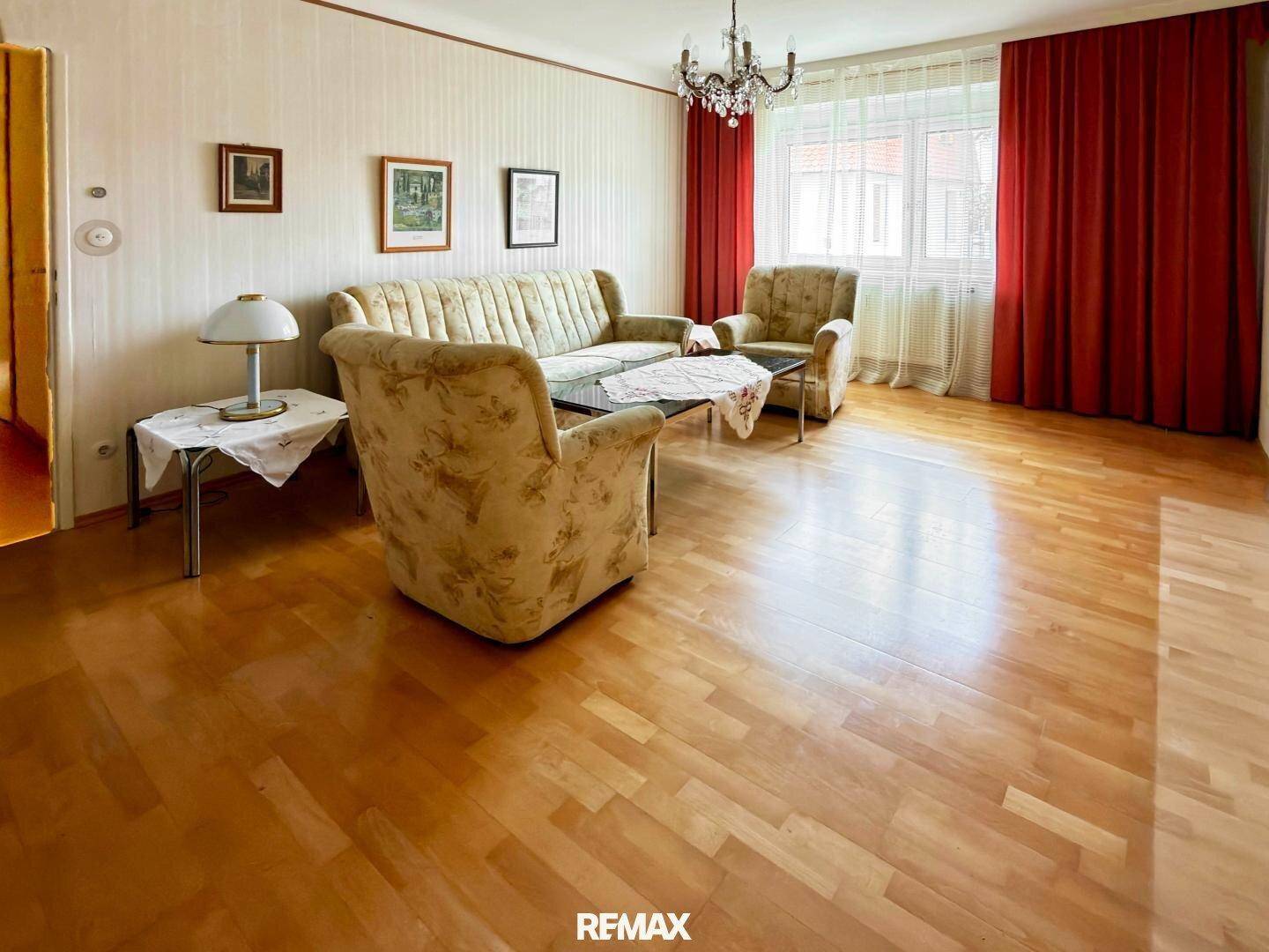 Gemütliches Wohnzimmer mit traditionellen Möbeln, Holzboden und roten Vorhängen.