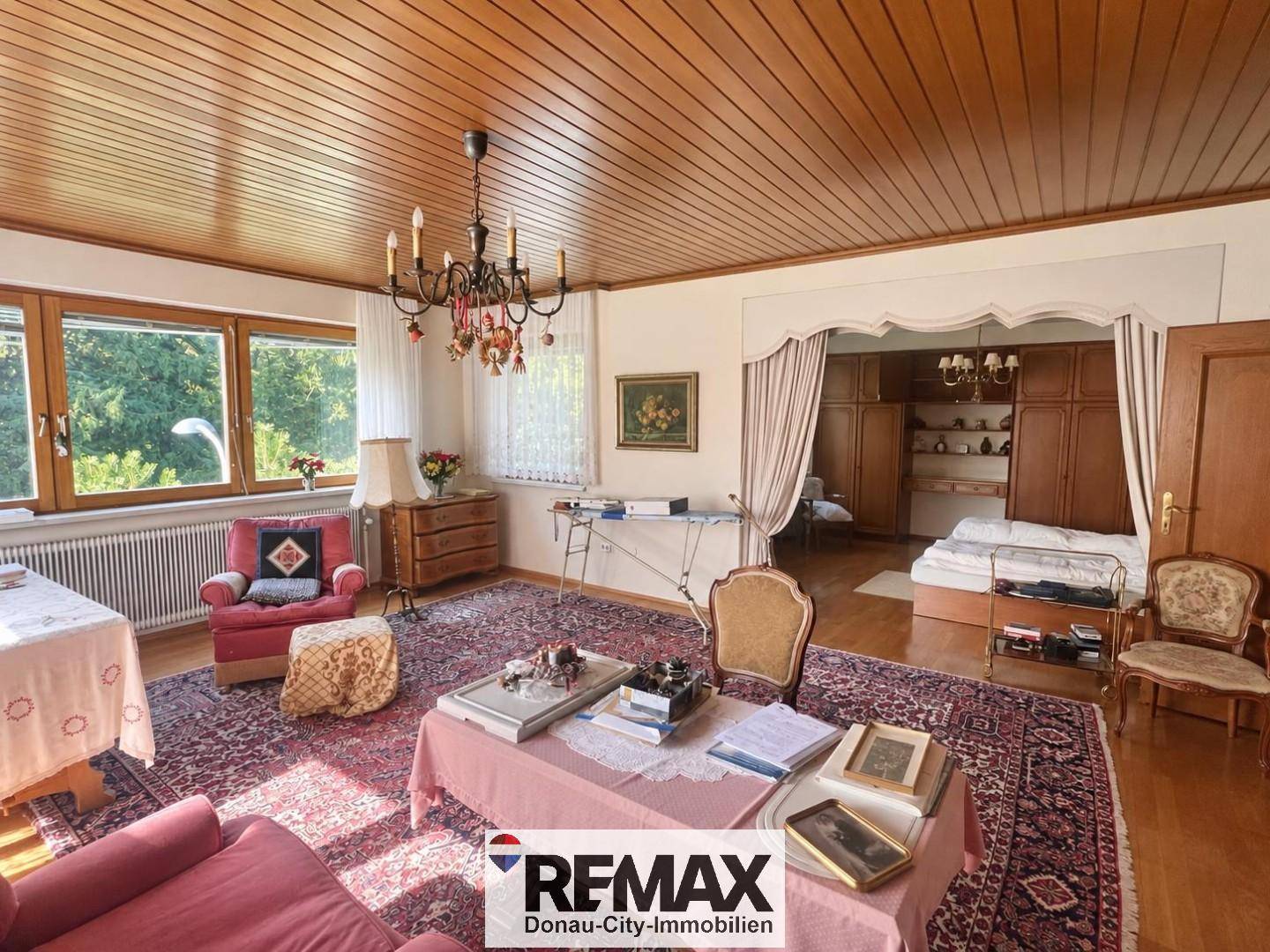 Gemütliches Wohnzimmer mit Holzdecke, traditionellen Möbeln und Blick ins Schlafzimmer.