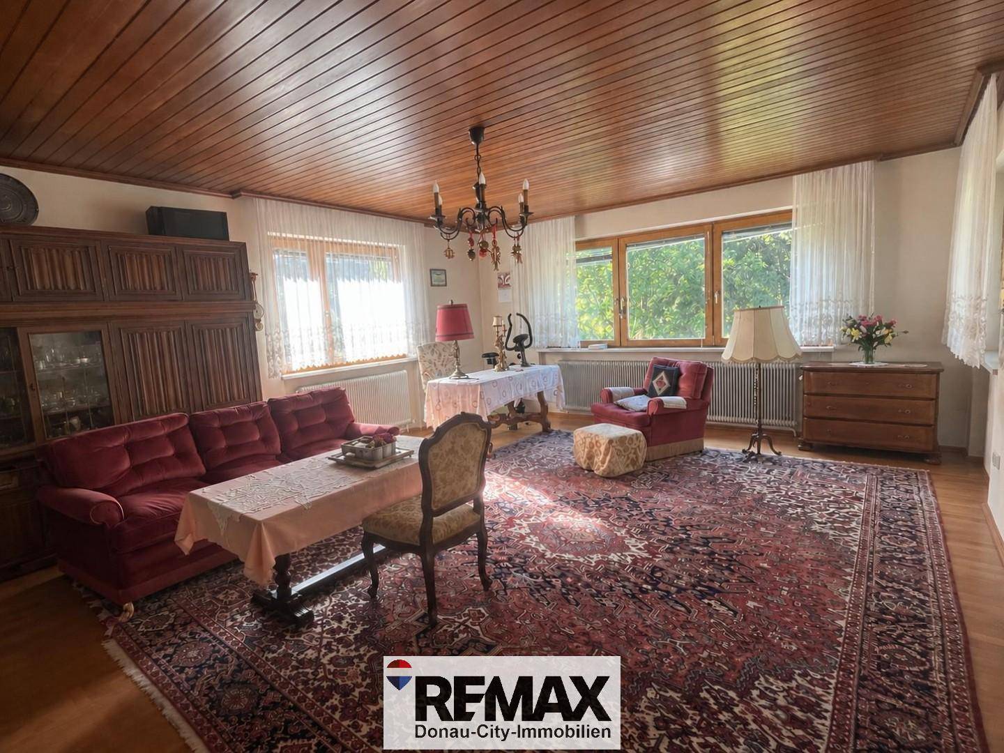 Geräumiges Wohnzimmer mit traditioneller Einrichtung, Holzdecke und großen Fenstern.