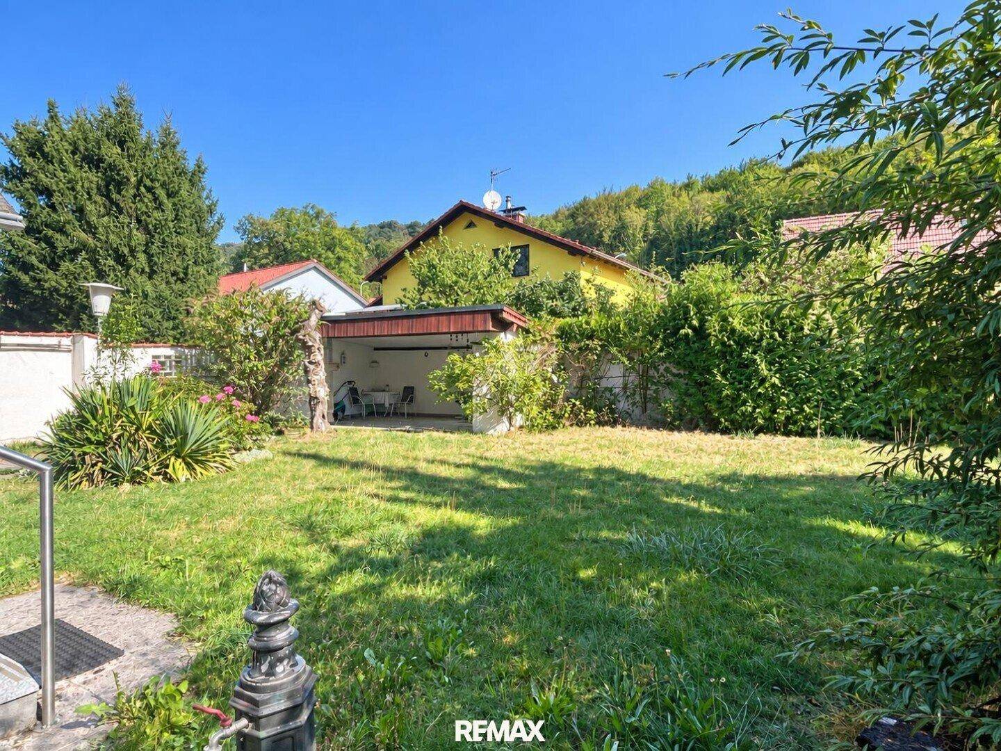 Hinterhof mit Rasenfläche, üppiger Hecke und einem überdachten Sitzbereich im Freien.
