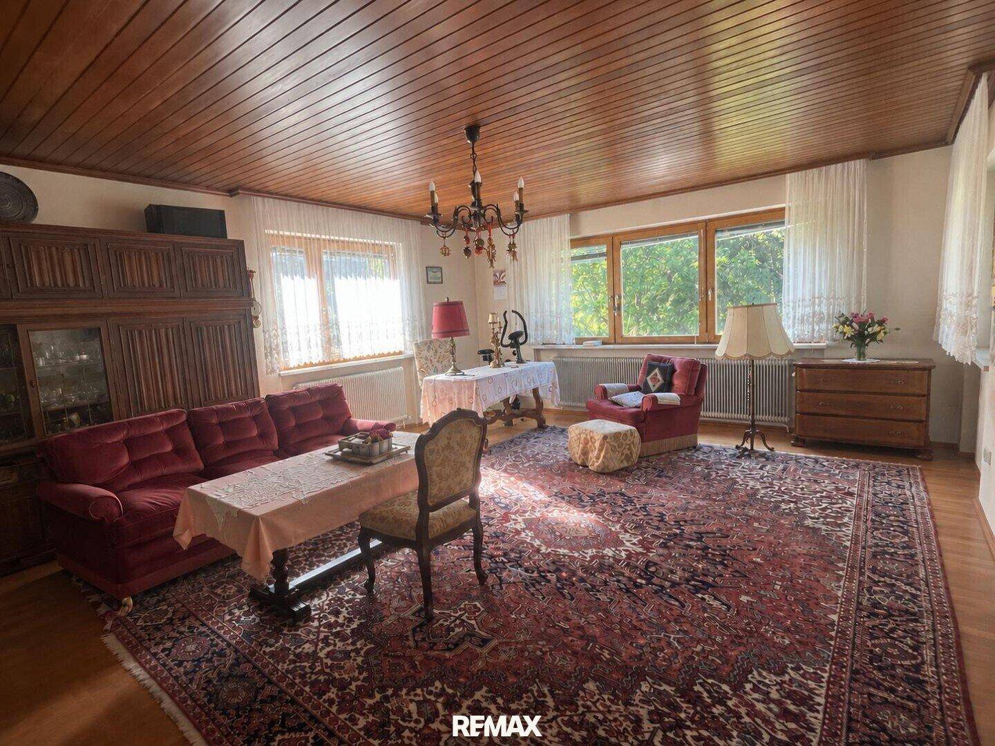 Geräumiges Wohnzimmer mit Holzdecke, traditionellen Möbeln und großen Fenstern.
