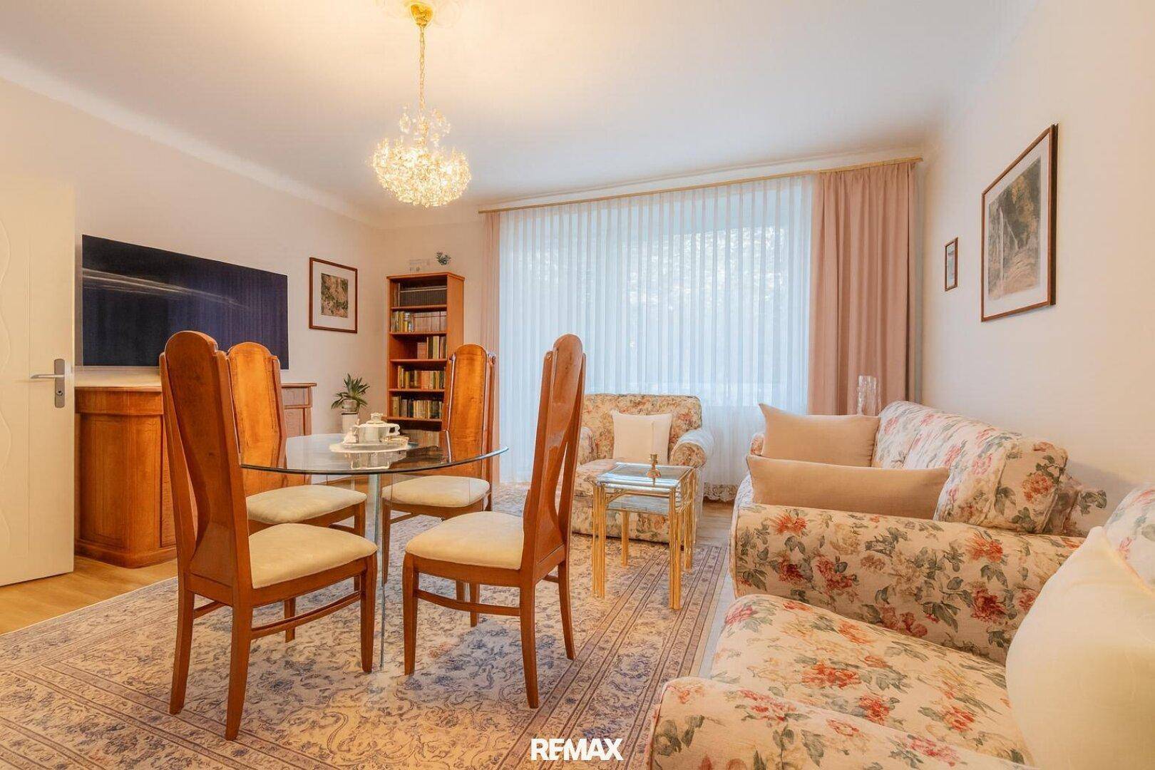 Klassisch eingerichteter Wohn-Essbereich mit floralen Sofas und einem eleganten Kronleuchter.