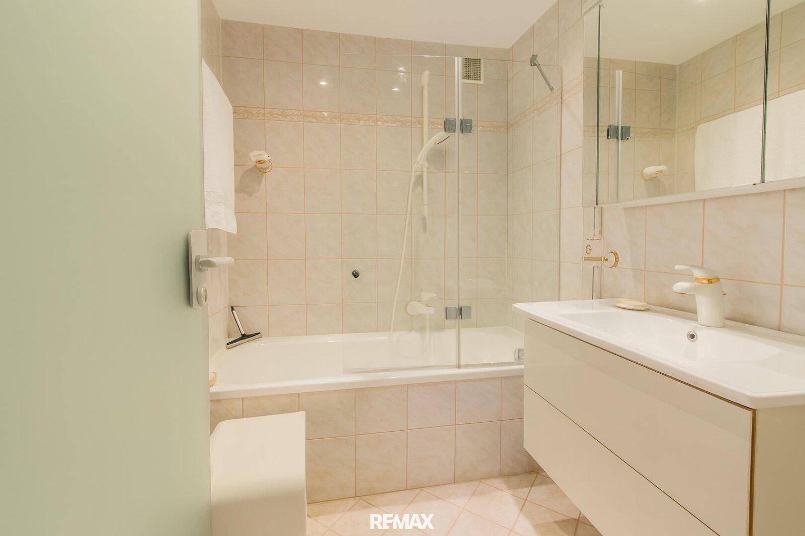 Gefliestes Badezimmer mit Badewanne, Duschabtrennung und Einzelwaschbecken in hellem Design.