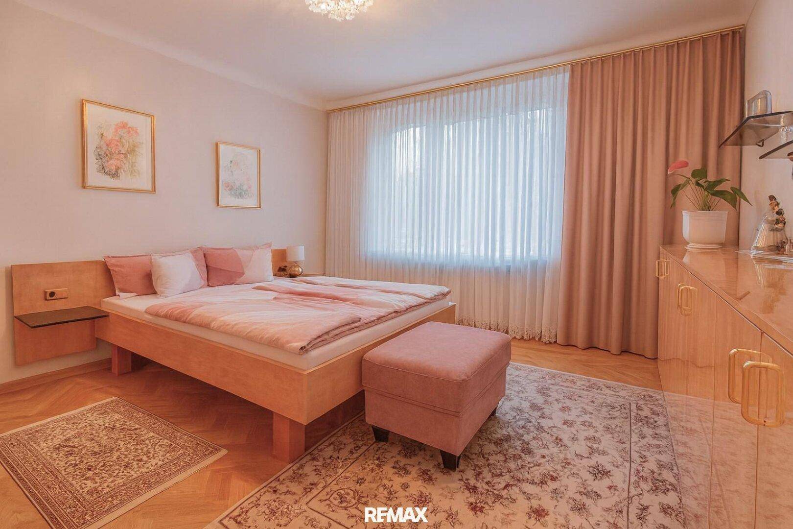 Schlafzimmer mit hellem Holzdoppelbett, Parkettboden und großem Fenster mit Vorhängen.