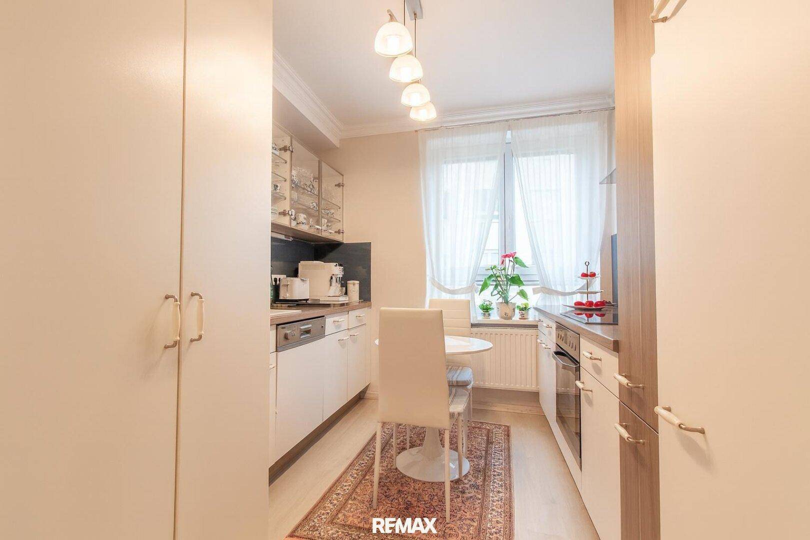 Funktionale Küche mit weißen Schränken, Essbereich und Fenster für natürliches Tageslicht.