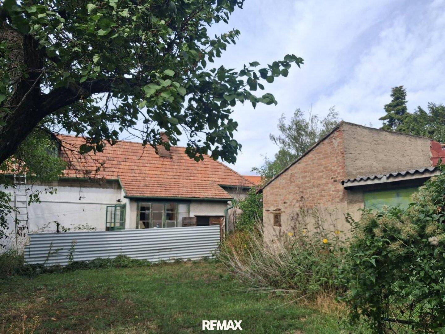Rückseite eines alten Hauses mit Ziegeldach und einem Nebengebäude im Garten.