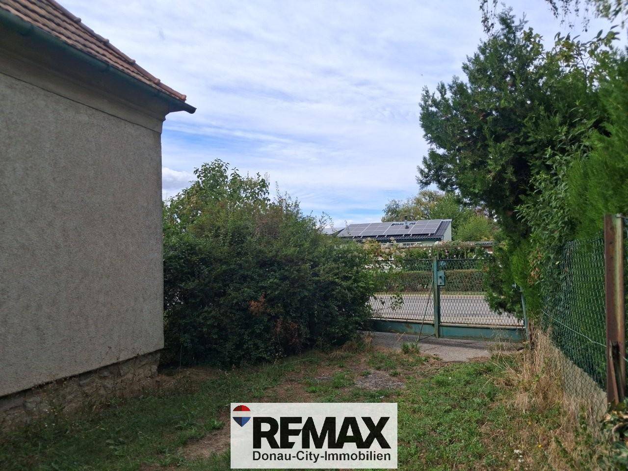 Seitenansicht des Hauses mit Zaun und im Hintergrund sichtbaren Solarmodulen auf einem Dach.