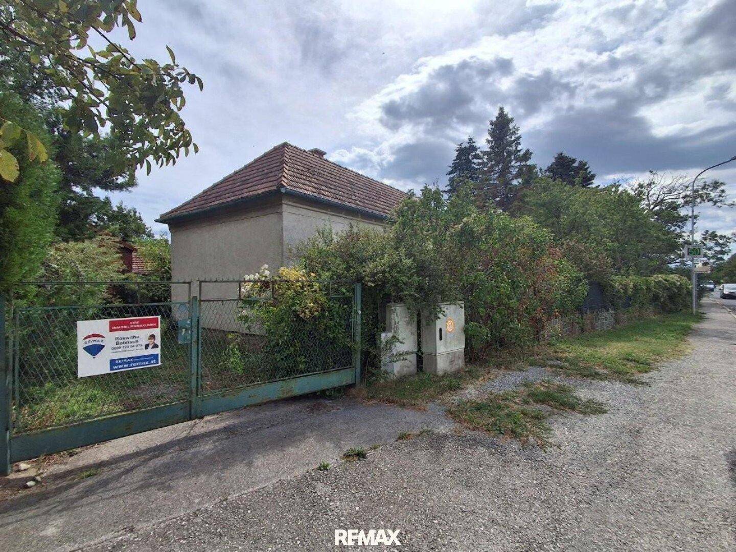 Altes Haus von der Straße aus gesehen, mit einem grünen Metalltor und üppiger Vegetation.