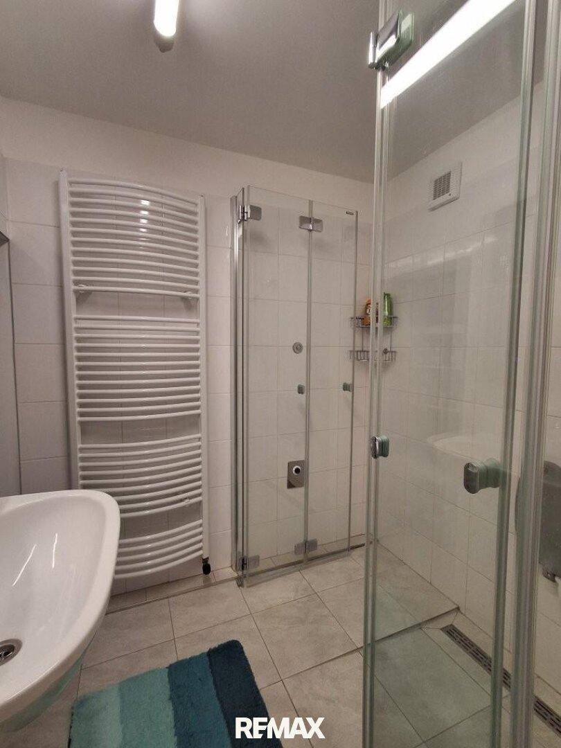 Helles Badezimmer mit geräumiger Duschkabine, modernen Fliesen und Heizkörper.