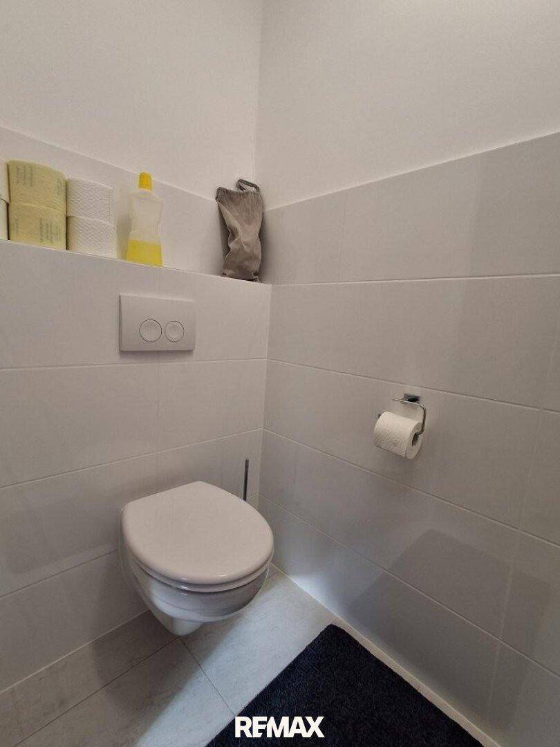 Separates Gäste-WC mit wandhängender Toilette und modernen weißen Fliesen.