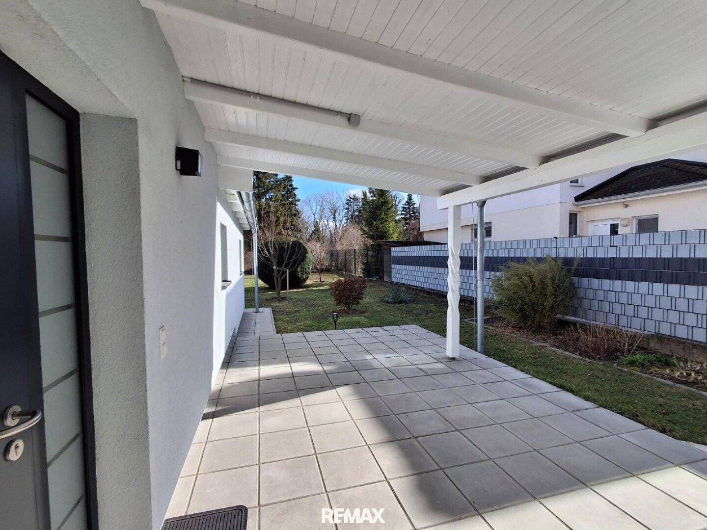 Überdachte Terrasse mit Fliesenboden und Zugang zum Garten, ideal für entspannte Stunden im Freien.