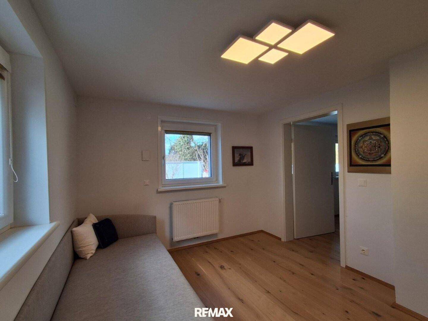Helles Schlafzimmer mit Holzboden, großem Fenster und einem bequemen Sofa.