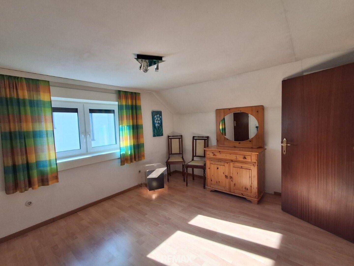 Gemütliches Schlafzimmer im Dachgeschoss mit Holzboden, Fenster und traditionellen Möbeln.