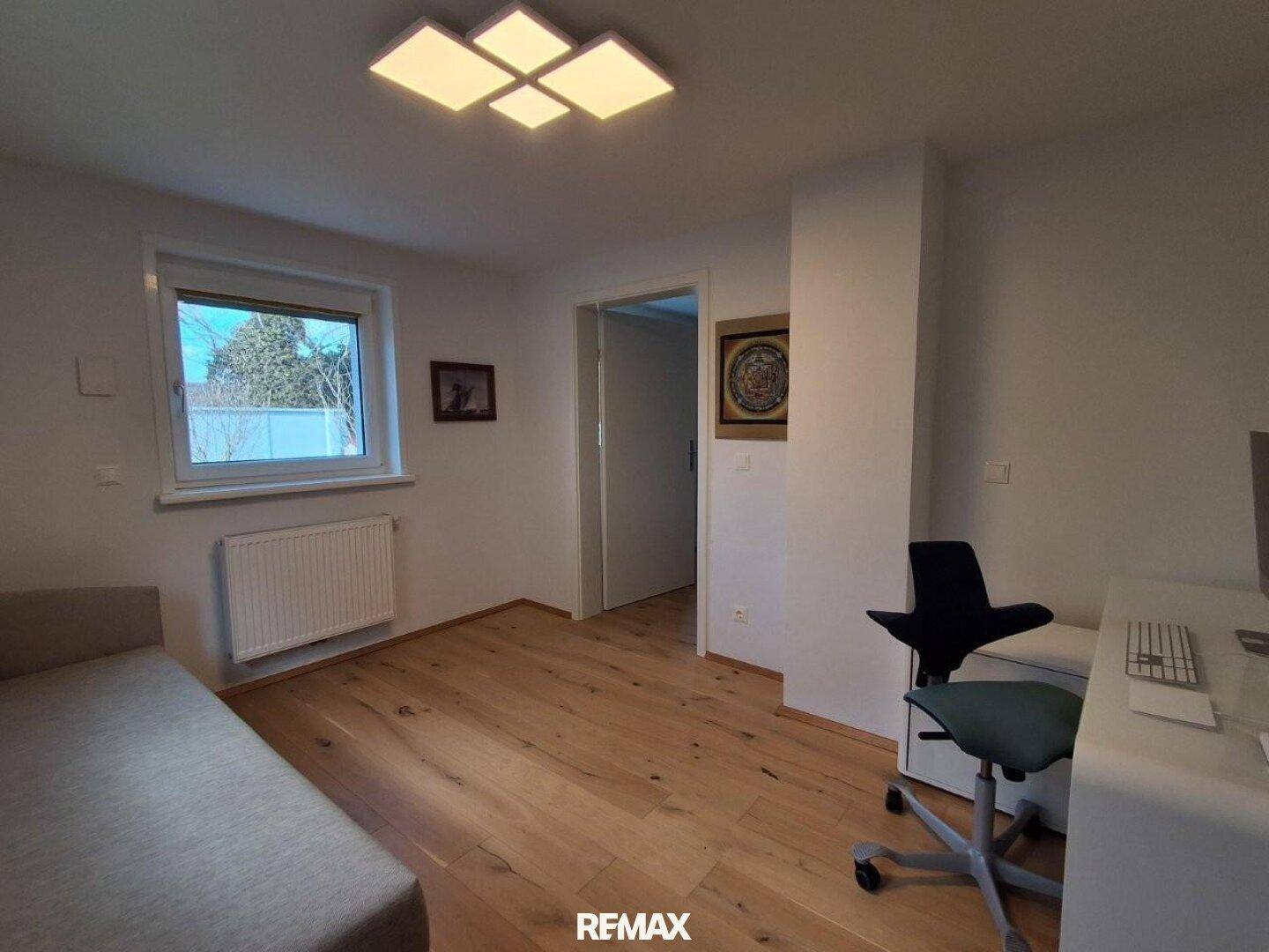Helles Schlafzimmer mit Holzboden, großem Fenster und einem Arbeitsbereich.